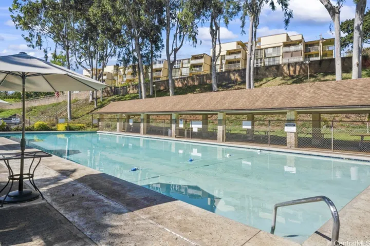 Another view of the community swimming pool featuring poolside seating and shaded areas.