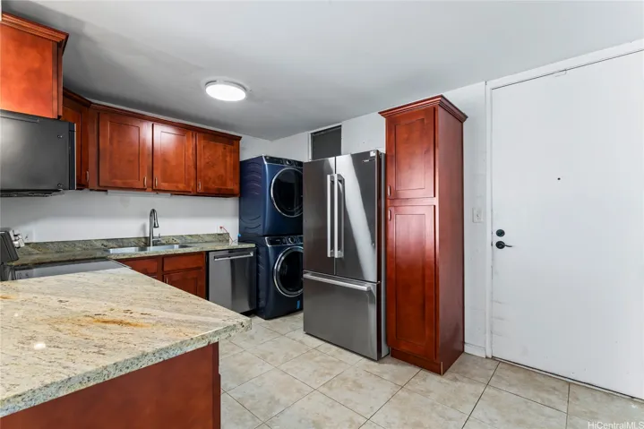 A functional kitchen with wood cabinetry, granite countertops, stainless steel appliances, and a stacked washer and dryer for added convenience.
