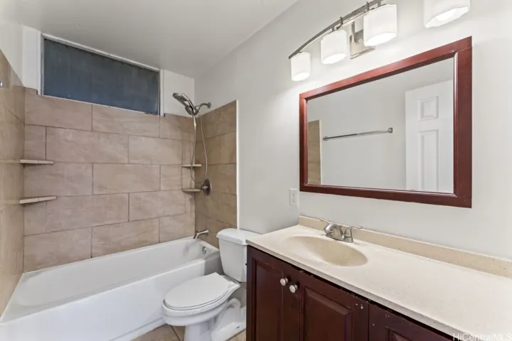 A full bathroom with a tub and shower combo, tile surround, single-sink vanity, and a large framed mirror with overhead lighting.
