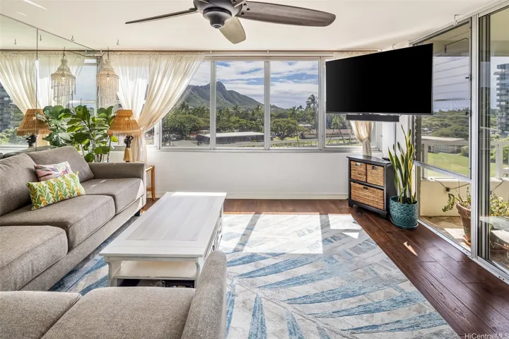 Light-filled living room viewed from the kitchen, showcasing Diamond Head and park views through expansive windows and easy flow out to the lanai.
