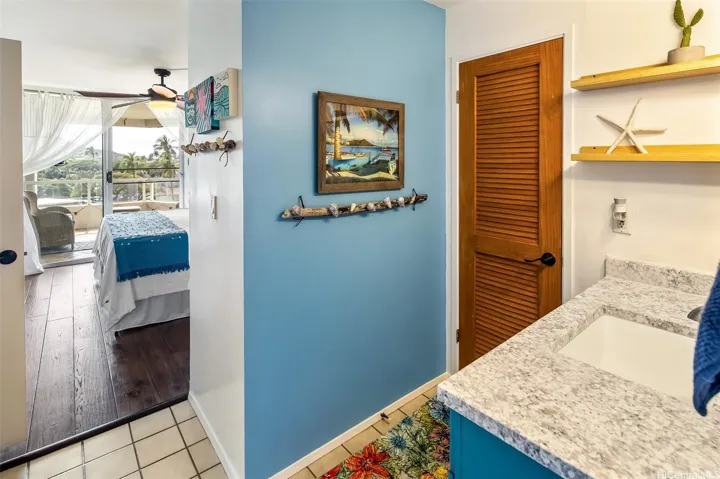Colorful primary en suite hallway with coastal accents, connecting the bedroom, vanity area, and bath, with a glimpse of the lanai and lush views beyond.