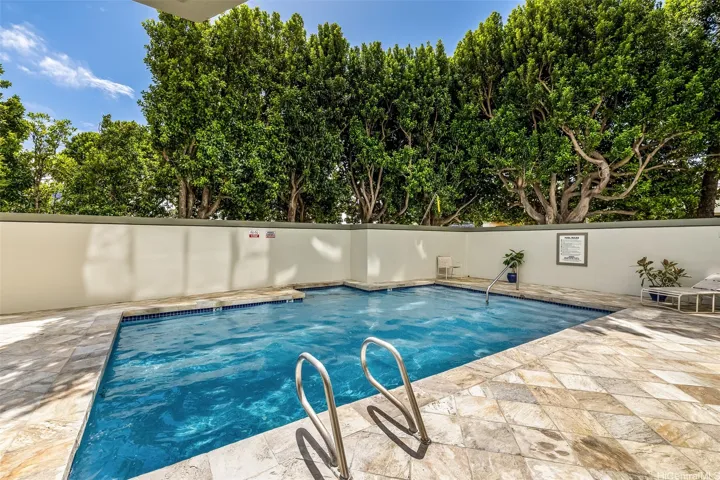 Inviting pool with sparkling water, lush privacy trees, and a sunny tiled deck perfect for relaxing or cooling off.