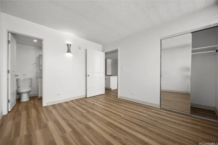 2BR/2BA: Spacious bedroom featuring mirrored closet doors, vinyl flooring, and adjacent bathroom.