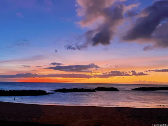 This image captures a breathtaking sunset over a calm shoreline, where vibrant hues of orange, pink, and violet stretch across the sky and reflect softly on the water