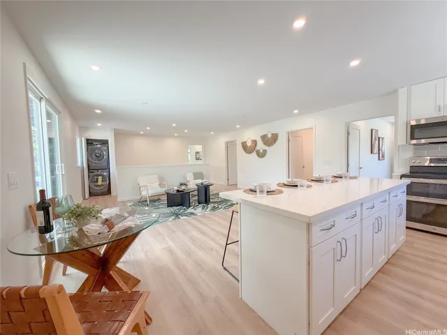 The kitchen overlooks a spacious open living area and features an extended island with quartz countertops, custom cabinetry, stainless steel appliances, and a large stacked washer and dryer for added convenience.