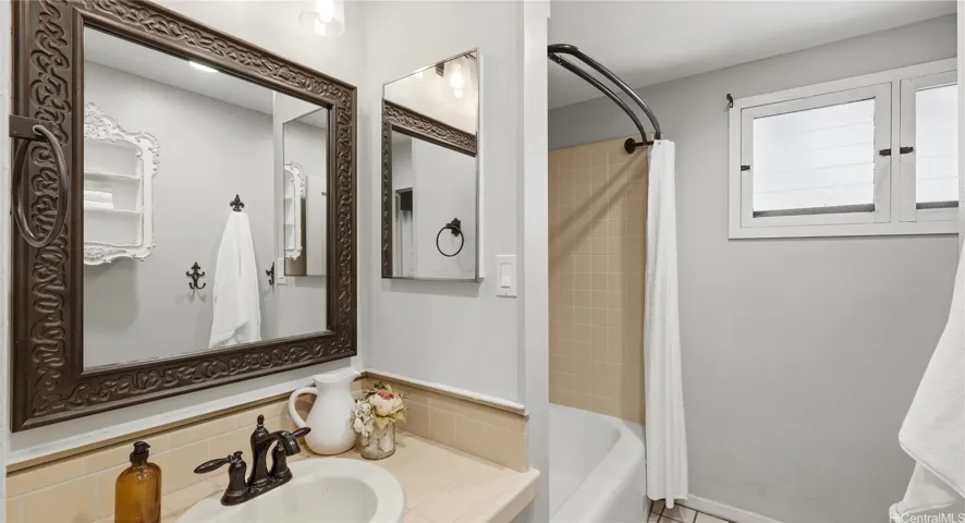 Full guest bathroom featuring a tiled vanity, shower/tub combo, and privacy window.