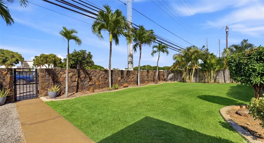 Securely walled and gated level yard featuring tropical palm trees and lush landscaping.