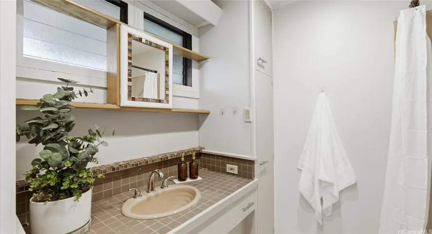 Private en-suite bathroom featuring a tiled vanity, built-in mirror, and convenient cabinet storage.