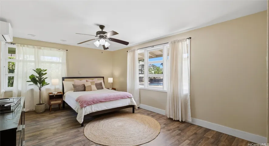 Main-level bedroom featuring split AC, a ceiling fan, and large windows overlooking the pool area.