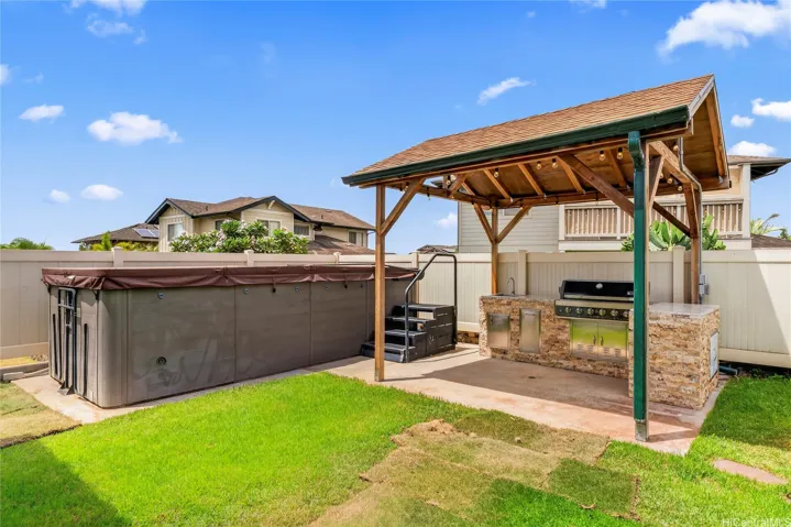 Backyard with a grassy lawn, covered grilling area, and a large swim spa.