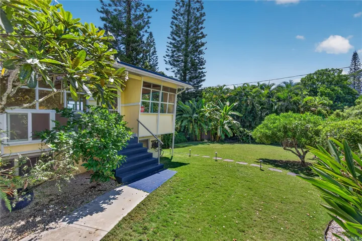 Lush and tropical food and flowers front yard. Pathways from the carport area and the street side front gate.