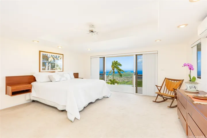 Serene primary bedroom on the lower, middle level, showcasing stunning panoramic views with sliding doors opening to a covered wraparound deck for seamless indoor-outdoor living.
