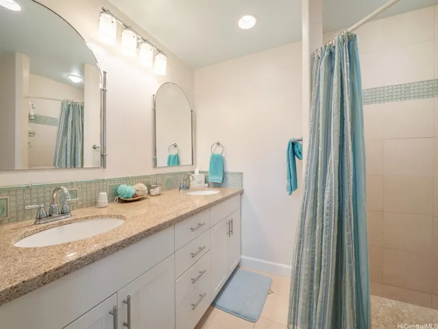 This private ensuite bathroom offers a bright, clean, and coastal-inspired design, creating a relaxing extension of the bedroom suite. The spacious double-sink vanity features granite countertops, abundant storage cabinetry, and elegant lighting, providing both style and functionality for daily routines. A large tiled walk-in shower with decorative accent tile adds a spa-like touch, while soft neutral finishes and thoughtful details enhance the serene atmosphere. Well-appointed and meticulously maintained, this ensuite bath delivers comfort, convenience, and privacy for the bedroom occupant.