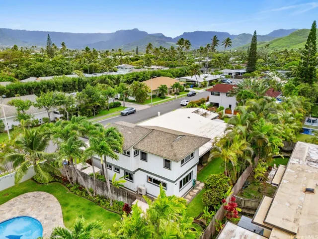 This impressive aerial view showcases the property's prime location within a lush, established neighborhood surrounded by tropical landscaping and dramatic mountain vistas. Nestled among mature palms and beautifully maintained homes, the residence offers a private setting while enjoying the natural beauty that makes Windward Oahu so desirable.