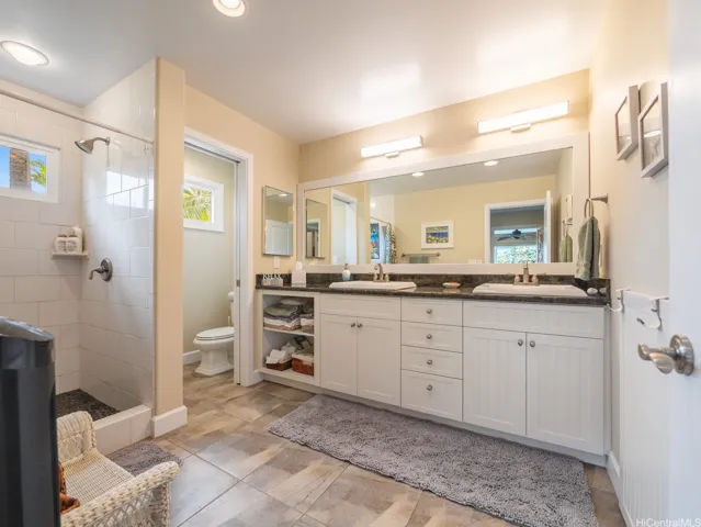 Designed to complement the private guest suite, this spacious bathroom offers comfort, convenience, and a bright, modern feel. The large double-sink vanity features elegant stone countertops, abundant cabinetry, and generous storage, making it ideal for extended stays. A walk-in tiled shower provides a clean, contemporary look, while the separate water closet enhances privacy and functionality. Thoughtfully appointed with ample lighting and quality finishes throughout, this well-designed bathroom serves as a comfortable retreat for guests and supports the suite's independent living arrangement. Combined with the guest suite's kitchenette, private lanai, and lock-off capability from the main home, this bathroom completes a truly private and self-contained guest quarters.