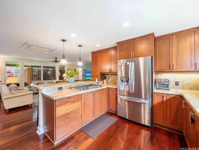This beautifully updated kitchen showcases a perfect blend of style and functionality, featuring rich wood cabinetry, gleaming granite countertops, and stainless steel appliances. The spacious peninsula with a built-in cooktop and bar seating creates a natural gathering place for family and guests, while abundant cabinet and counter space make meal preparation a pleasure. Warm hardwood flooring flows throughout the open-concept layout, connecting the kitchen seamlessly to the living and dining areas. Thoughtfully designed for both everyday living and entertaining, this inviting space offers the ideal setting for modern island living.