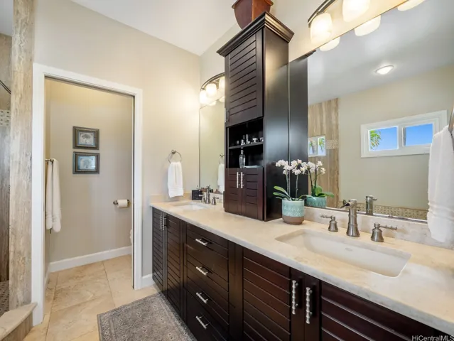 The expansive dual-sink vanity features rich custom cabinetry, generous counter space, and a built-in storage tower, providing exceptional organization for everyday living. High-end finishes, abundant lighting, and a large mirror enhance the bright and airy atmosphere.