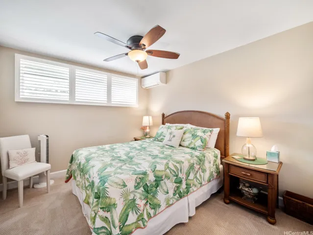 This comfortable and inviting bedroom offers a peaceful retreat with soft natural light, neutral tones, and plush carpeting underfoot. Plantation shutters provide privacy while enhancing the room's clean, island-inspired design. The spacious layout comfortably accommodates a queen-sized bed and furnishings, while the split-system air conditioning and ceiling fan ensure year-round comfort. A generously sized walk-in closet provides ample storage and organization space, making this well-appointed bedroom both functional and relaxing for residents or guests alike.