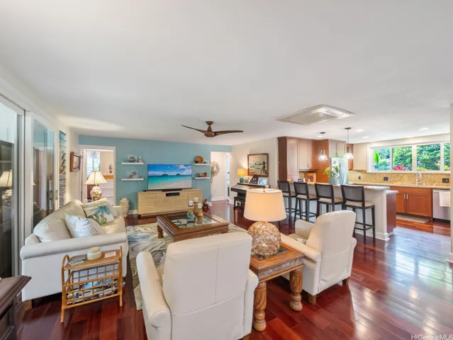 This open-concept great room seamlessly connects the living, dining, and kitchen areas. Rich hardwood flooring adds warmth and elegance throughout, while large windows and sliding glass doors invite abundant natural light and create a smooth transition to the covered lanai. The updated kitchen features generous counter space, quality cabinetry, and a large breakfast bar with seating, making it ideal for both everyday living and entertaining. The comfortable living area offers a welcoming gathering space, all enhanced by a thoughtful layout that embraces Hawaii's indoor-outdoor lifestyle.