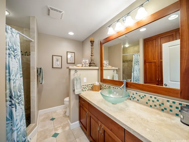 Conveniently located to serve two secondary bedrooms and guests, this beautifully updated bathroom combines comfort and functionality with tasteful island-inspired finishes. The spacious vanity features rich wood cabinetry, a vessel sink, and generous counter space, complemented by a large framed mirror and stylish accent tile backsplash. The tiled walk-in shower adds a touch of luxury, while ample storage ensures everyday convenience. Thoughtfully designed and well-appointed, this bathroom provides an attractive and practical space for family members and visitors alike.