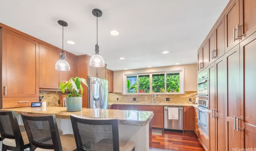 The heart of the home, this beautifully designed kitchen combines style and functionality with an open layout perfect for everyday living and entertaining. Rich wood cabinetry, granite countertops, and stainless steel appliances create a warm and timeless aesthetic, while the expansive island with bar seating provides plenty of space for casual dining, meal preparation, and gathering with guests. Large windows frame lush garden views and fill the space with natural light, enhancing the bright and inviting atmosphere. Seamlessly connected to the living area, this kitchen is perfectly suited for modern island living and effortless entertaining.