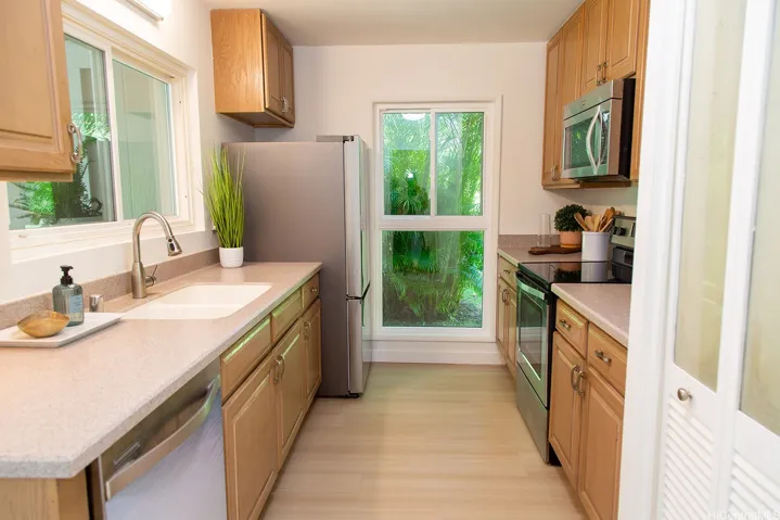 This well-designed kitchen features generous cabinetry, stainless steel appliances, a pantry, a large end-unit window for beautiful natural light, and a lovely window overlooking the lanai. | Enhanced