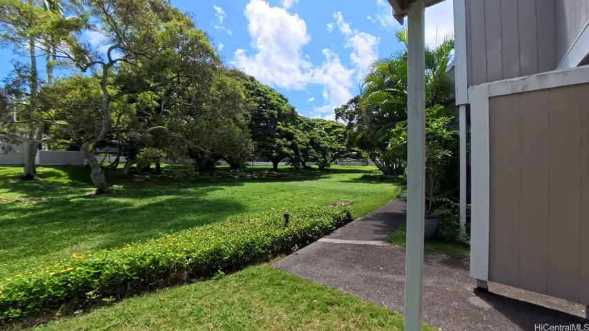 Step outside and enjoy the expansive grassy area behind the unit, offering a peaceful, open setting surrounded by mature trees and tropical greenery. | Enhanced