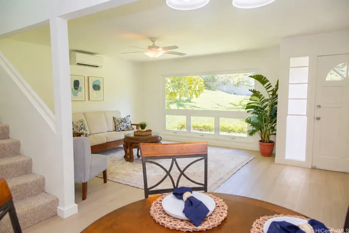 Natural light pours into this inviting main living space, where expansive windows frame the surrounding greenery and the back door opens directly to the large greenspace behind, all with an easy flow into the dining area and the comfort of split AC. | Enhanced