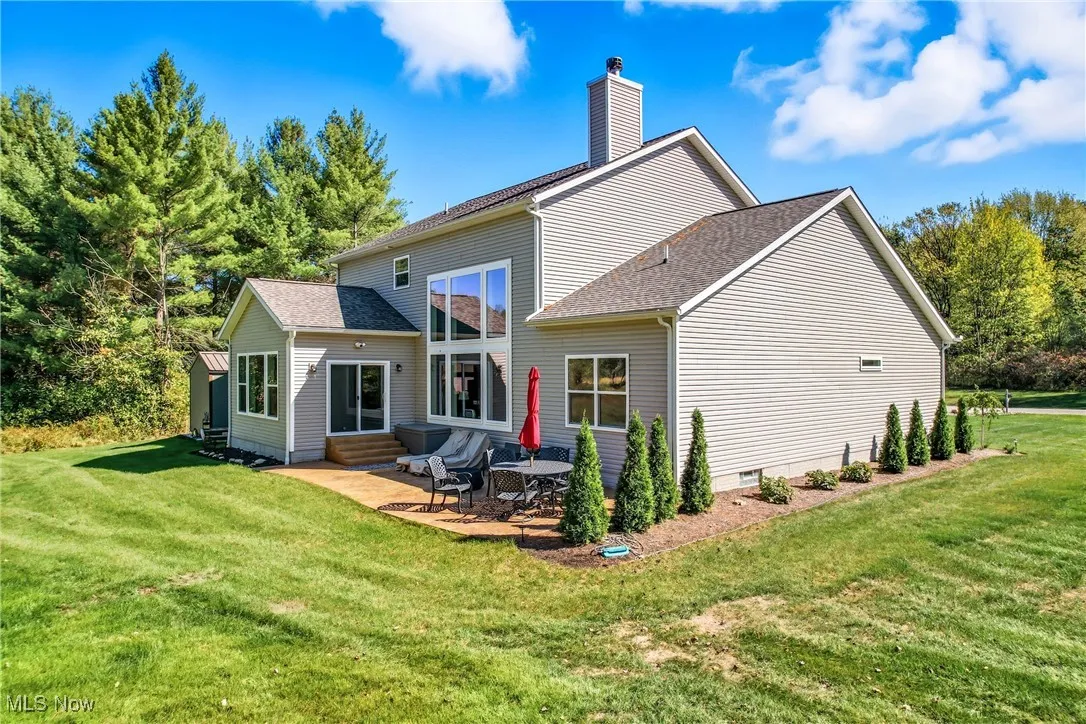 Back of house featuring a shingled roof, a lawn, a chimney, and a patio