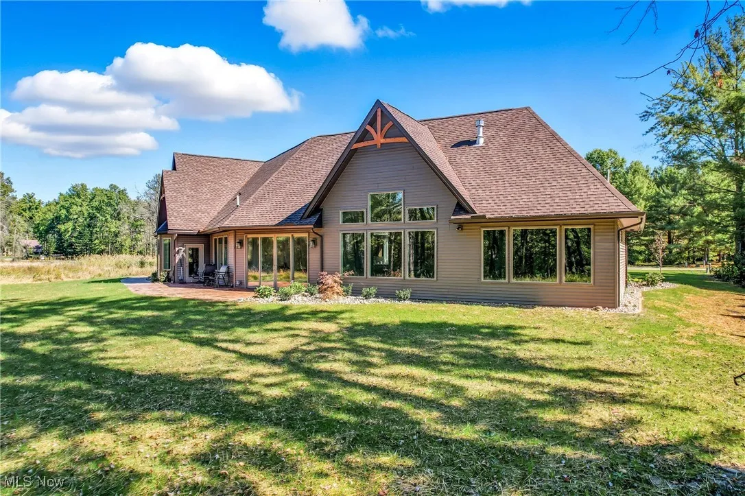 Rear view of property featuring a patio area, a yard, and a shingled roof