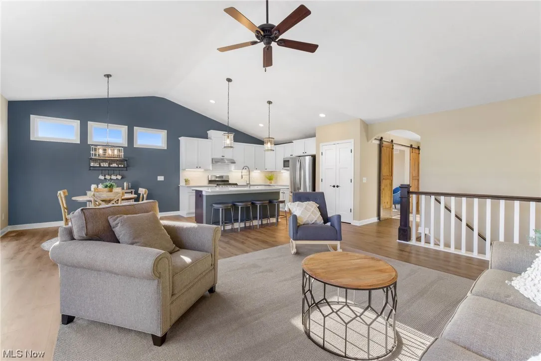 Living room with lofted ceiling, sink, ceiling fan, and light hardwood floors