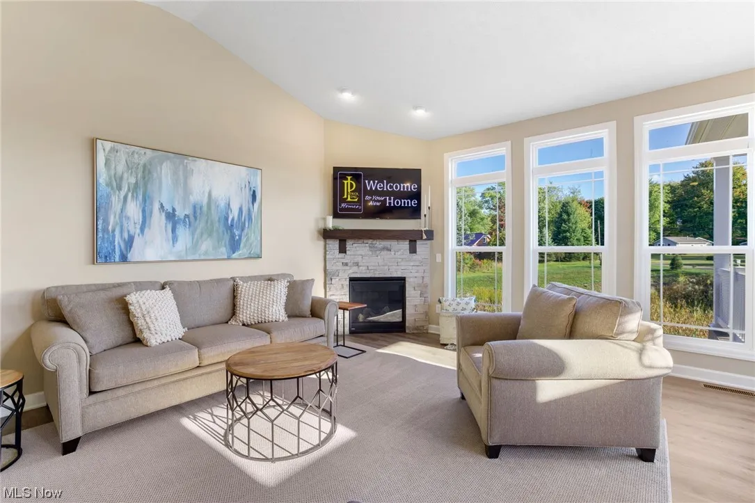 Living room with lofted ceiling, light hardwood floors, and a stone fireplace