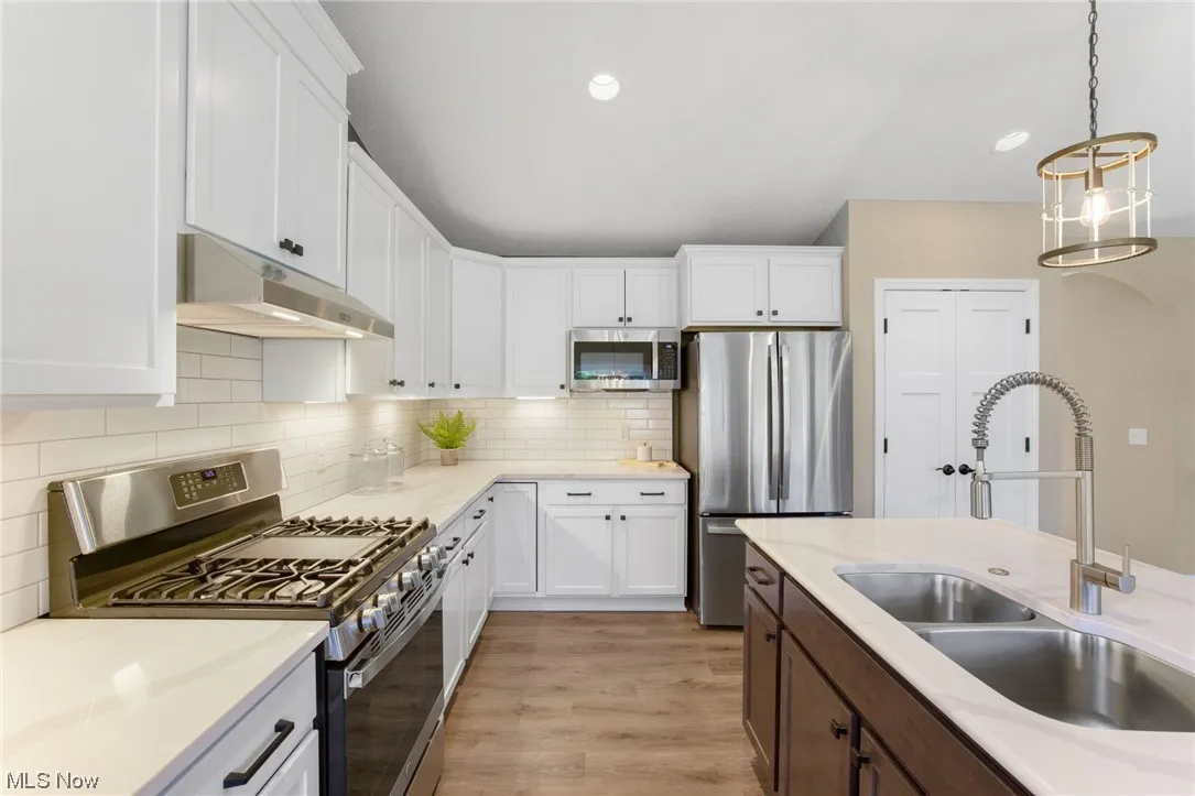 Kitchen featuring decorative light fixtures, tasteful backsplash, light hardwood floors, appliances with stainless steel finishes, and white cabinetry