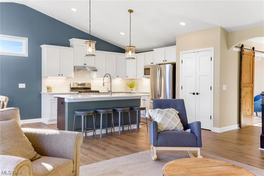 Living room with a barn door, sink, vaulted ceiling, and light hardwood flooring