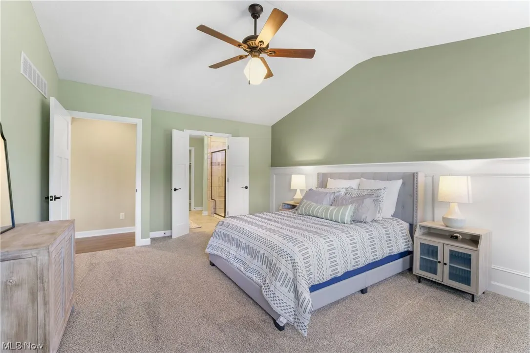 Carpeted bedroom with vaulted ceiling, ceiling fan, and connected bathroom