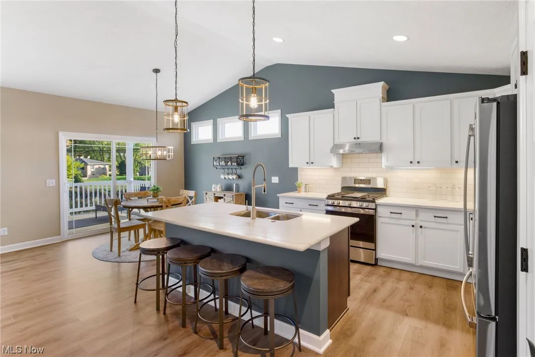 Kitchen featuring decorative light fixtures, vaulted ceiling, an island with sink, stainless steel appliances, and sink
