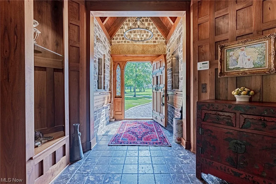 Doorway to outside with vaulted ceiling, wooden walls, dark tile floors, and a chandelier