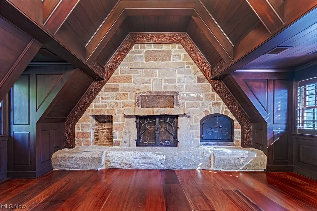 Unfurnished living room with wood ceiling, dark hardwood floors, and a stone fireplace