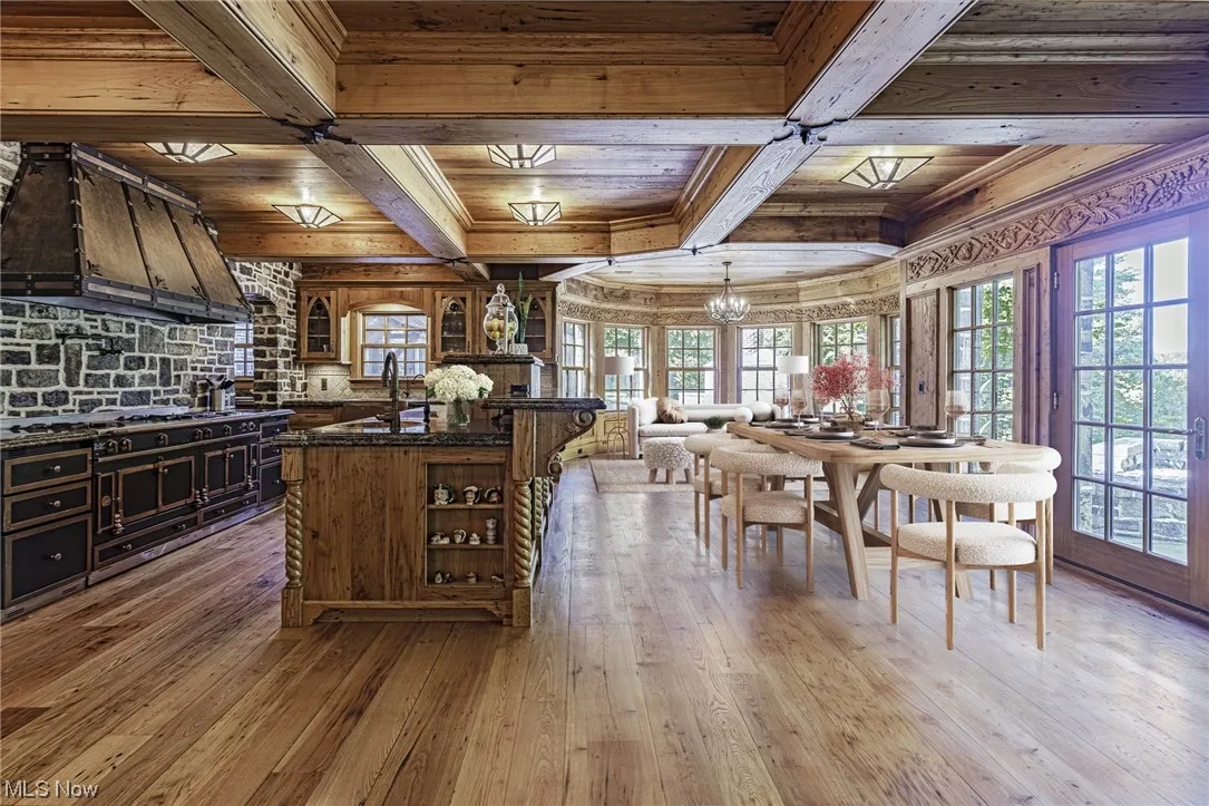Kitchen featuring hardwood flooring, dark stone counters, an inviting chandelier, a kitchen island with sink, and decorative light fixtures