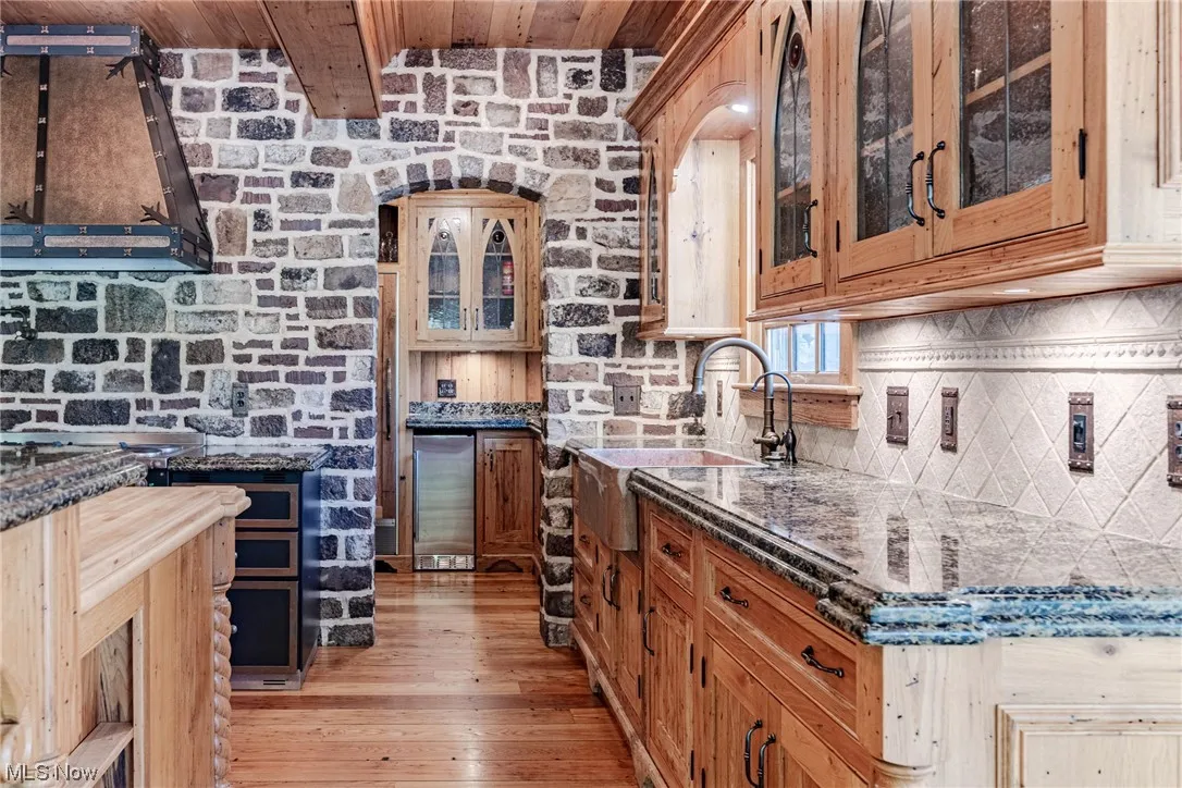 Kitchen with backsplash, dark stone counters, brick wall, and light hardwood flooring
