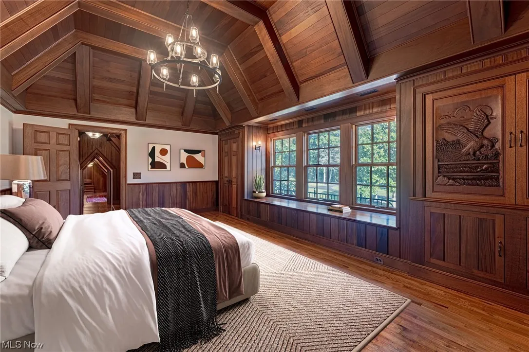 Bedroom with vaulted ceiling with beams, a chandelier, light hardwood floors, wooden ceiling, and wood walls