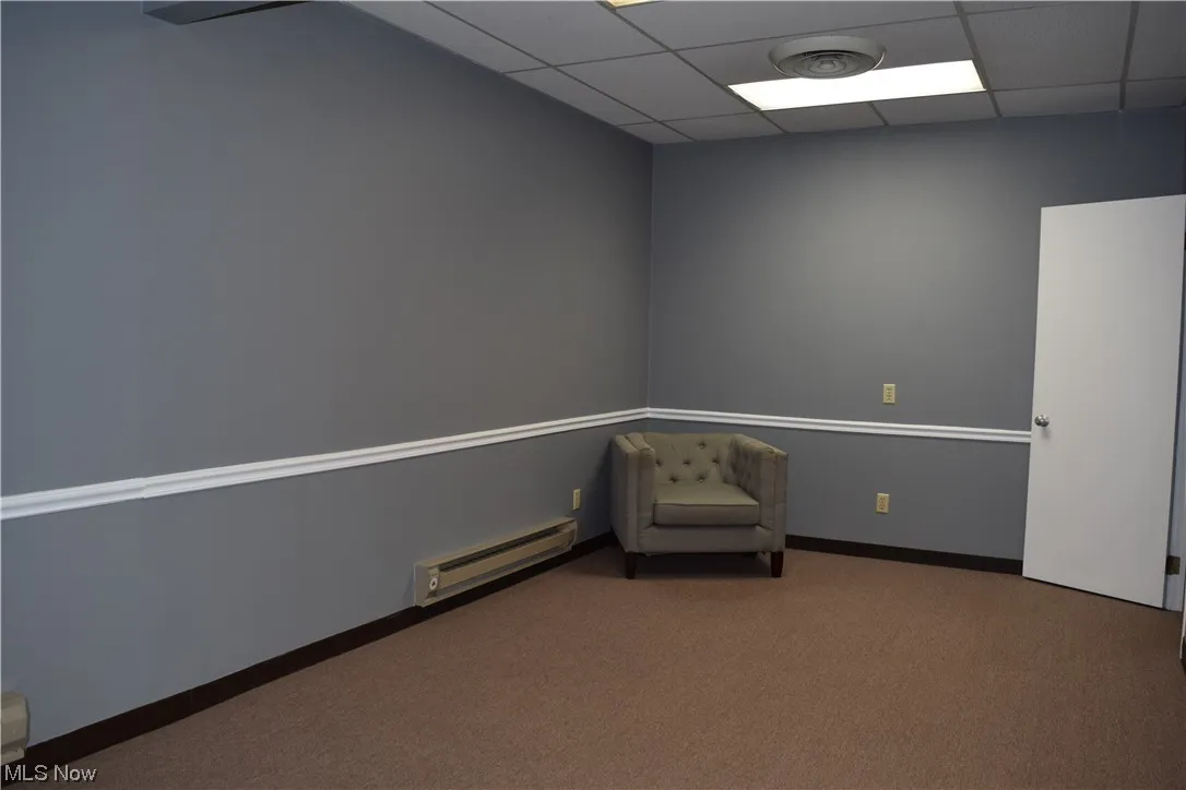 Living area with a paneled ceiling, dark carpet, and a baseboard radiator