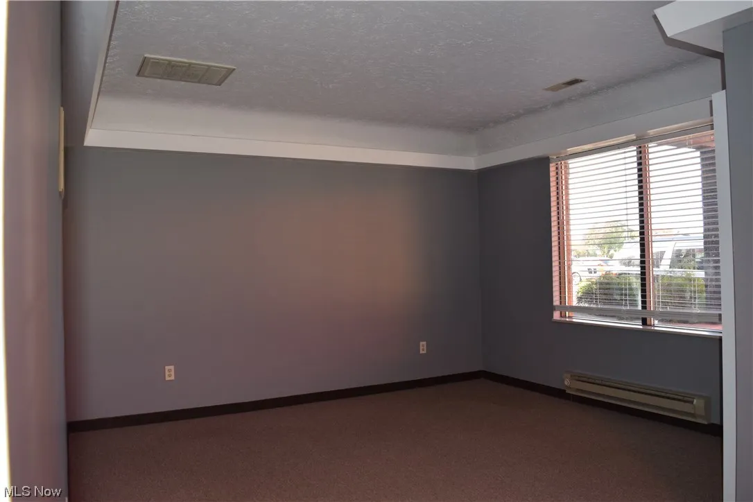 Carpeted empty room featuring a textured ceiling and a baseboard radiator
