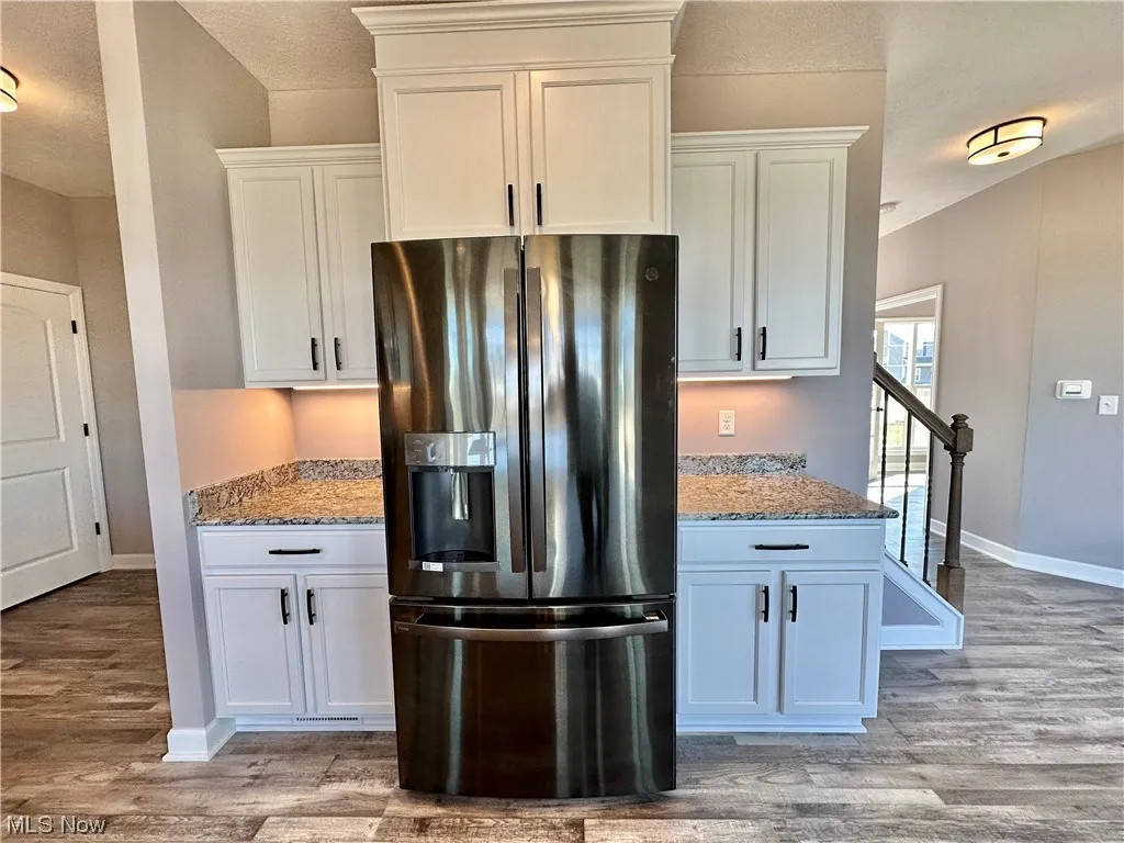 Kitchen with black fridge, light stone countertops, light wood-type flooring, and white cabinetry