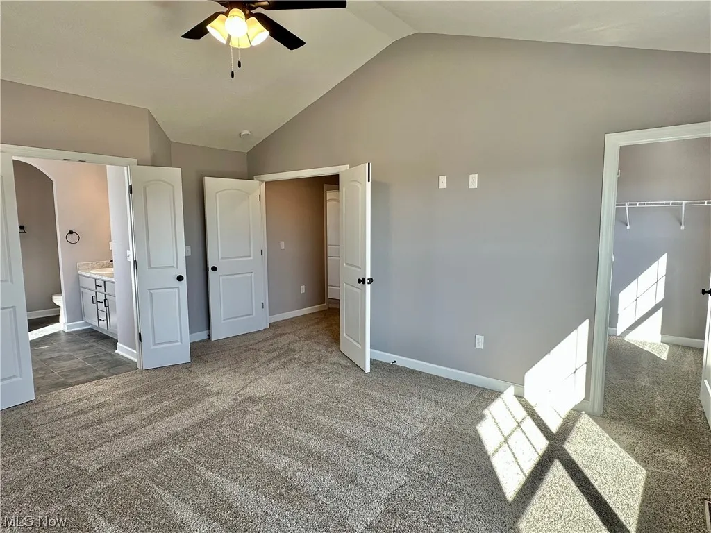 Unfurnished bedroom with dark carpet, a closet, ensuite bath, ceiling fan, and a spacious closet