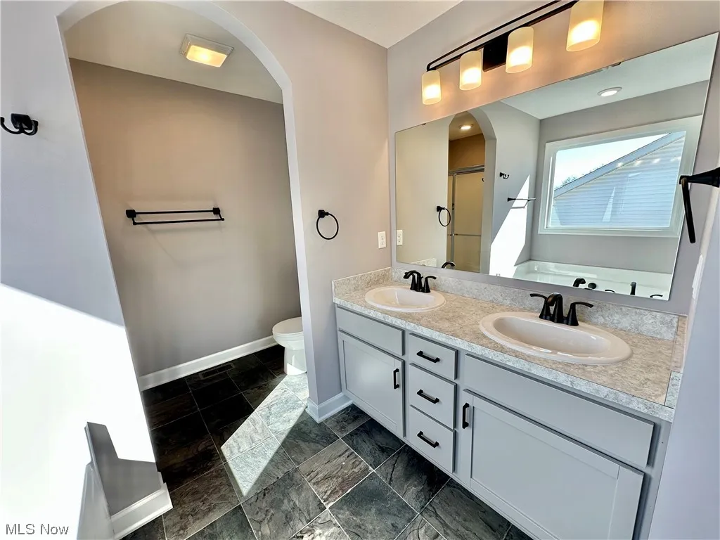 Bathroom featuring toilet, a bathtub, oversized vanity, dual sinks, and tile flooring
