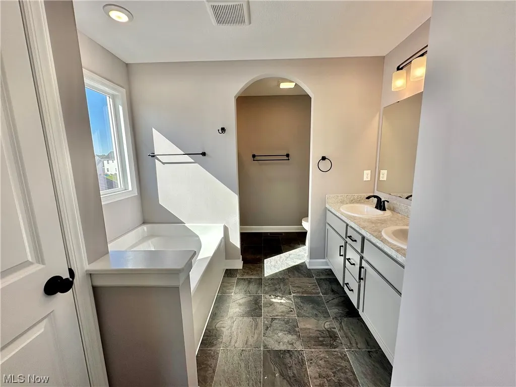 Bathroom featuring toilet, a bathing tub, tile flooring, and dual bowl vanity