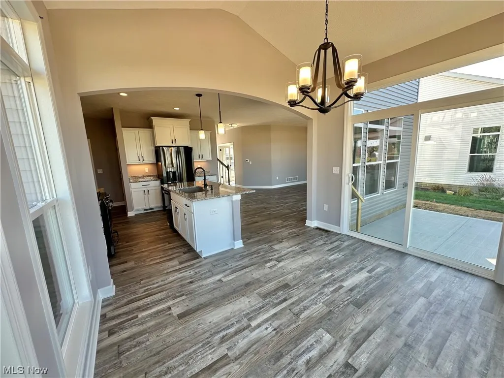 Kitchen with an inviting chandelier, pendant lighting, dark hardwood / wood-style flooring, a center island with sink, and white cabinetry
