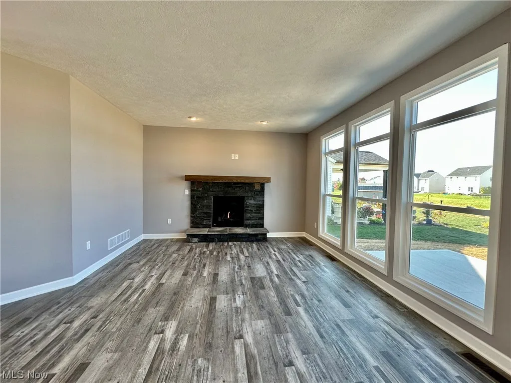 Unfurnished living room featuring a textured ceiling, dark hardwood / wood-style flooring, and a stone fireplace