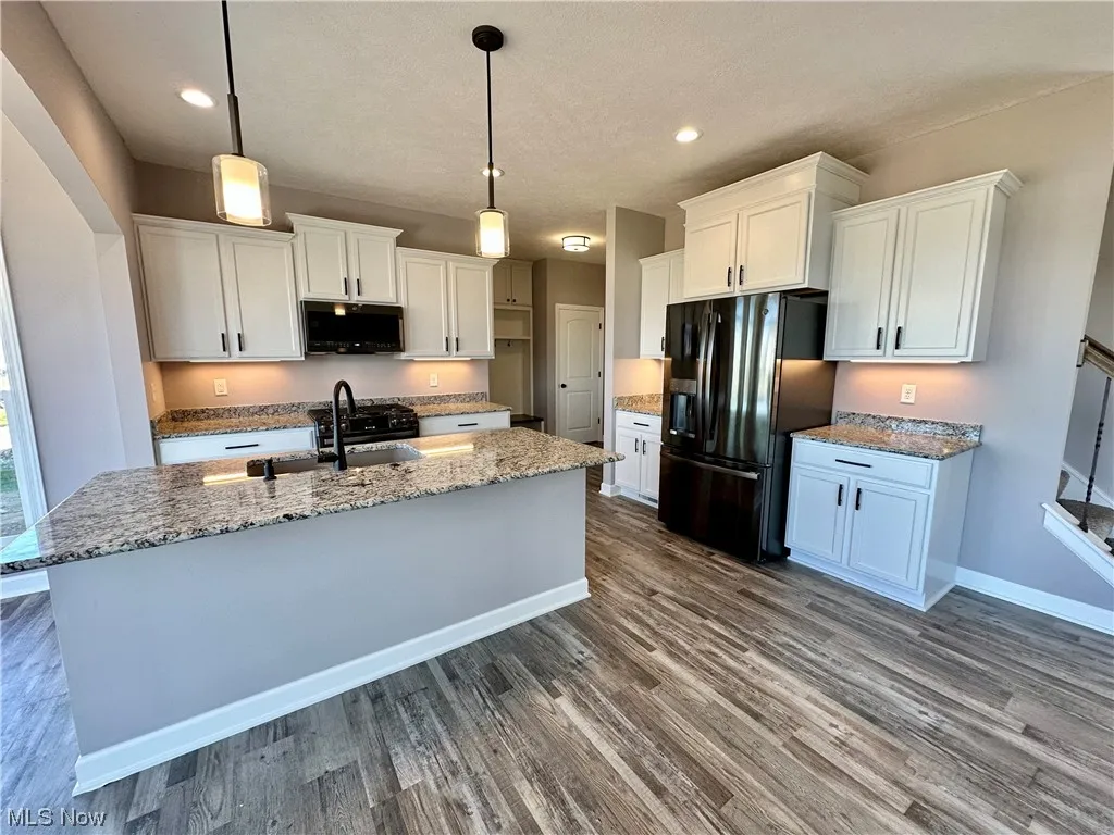 Kitchen with black appliances, hanging light fixtures, and a kitchen island with sink